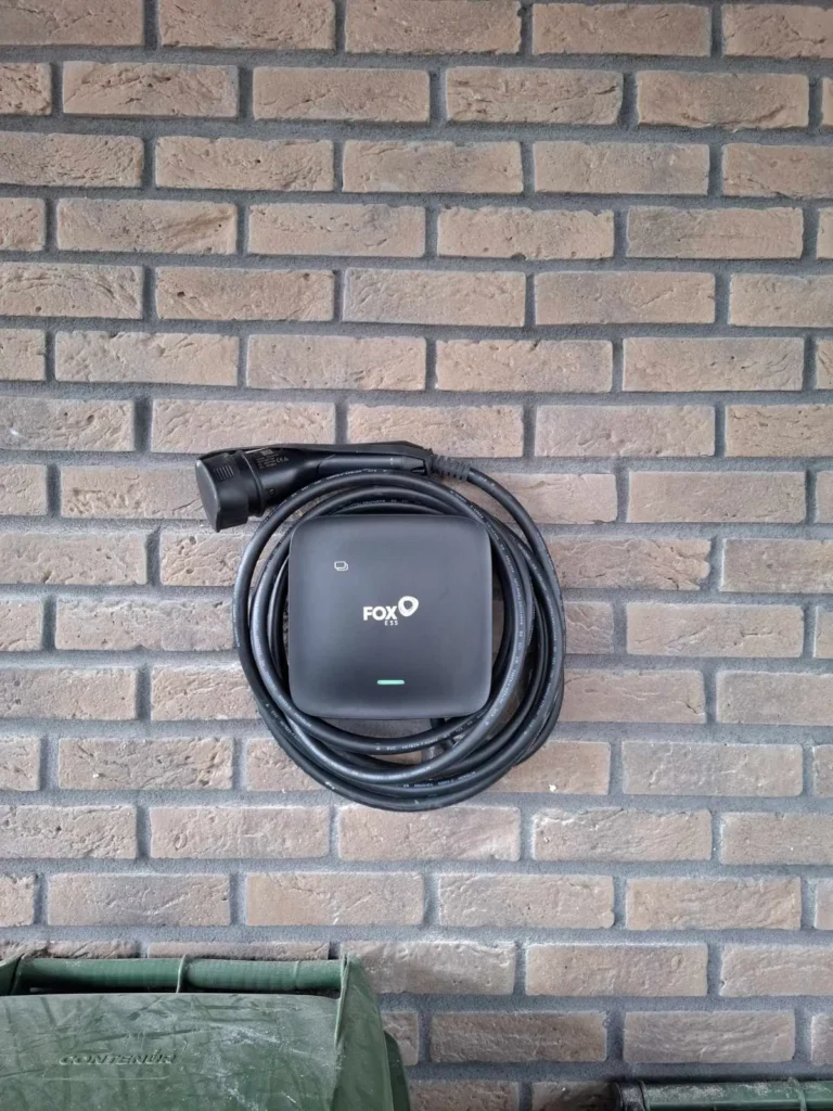 FoxESS elektromobilio įkrovimo stotelė su pakabintu kabeliu ant plytų sienos