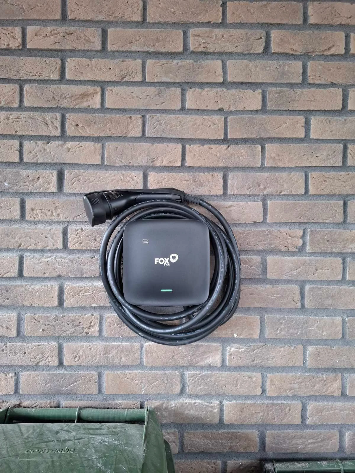 FoxESS elektromobilio įkrovimo stotelė su pakabintu kabeliu ant plytų sienos
